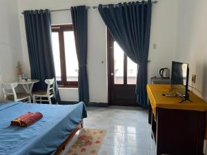 1 dormitorio con 1 cama con cortinas azules y escritorio en Tulip Mui Ne en Phan Thiet