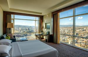 um quarto de hotel com uma cama e uma grande janela em The Biltmore Tbilisi Hotel em Tbilisi