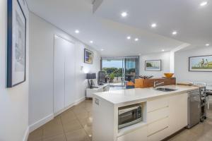 Il comprend une cuisine ouverte et un salon aux murs blancs. dans l'établissement Casuarina Resort Style 3BR Apartment by uHoliday, à Casuarina