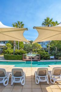 un groupe de chaises et de parasols à côté d'une piscine dans l'établissement Casuarina Resort Style 3BR Apartment by uHoliday, à Casuarina