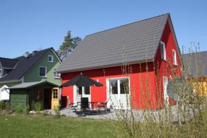 a red and green house with a table and an umbrella at K77 - 5 Sterne Ferienhaus mit Sauna, grossem Garten direkt am See in Roebel an der Mueritz in Marienfelde