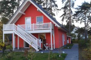 uma casa vermelha com um deque branco e escadas em K 104 OG - stilvolle Ferienwohnung am See mit Balkon & Sauna in Röbel an der Müritz em Marienfelde