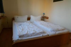 uma cama com lençóis brancos e almofadas em 30 EG - Gemuetliche Ferienwohnung direkt am See in Roebel Mueritz em Marienfelde