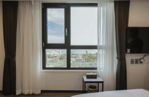 een slaapkamer met een groot raam met witte gordijnen bij Lemain Hotel Seogwipo in Seogwipo