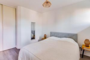 a white bedroom with a bed and a chandelier at Sejour au coeur du Bassin d Arcachon avec jardin in Lanton