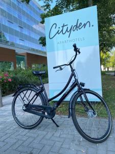 un vélo garé à côté d'un panneau devant un bâtiment dans l'établissement Cityden Zuidas, à Amstelveen