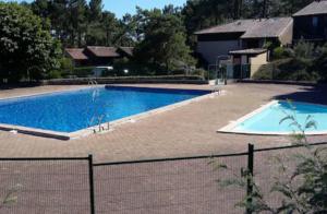 a large swimming pool next to a fence at Petite maison au cœur de la pinède in Lacanau
