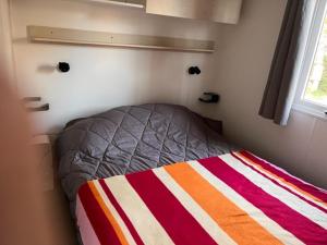 Ce lit se trouve dans une petite chambre dotée d'une couette à rayures. dans l'établissement Mobil home Clim, Tv - Camping Falaise Narbonne Plage 4 étoiles - 004, à Narbonne-Plage