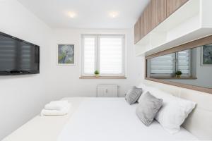 a white bedroom with a large bed and a flat screen tv at Sunny Kliny Apartment in Krakow