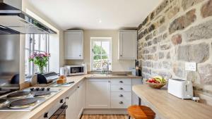 a kitchen with white cabinets and a stone wall at Hobcroft Cottage in Warslow