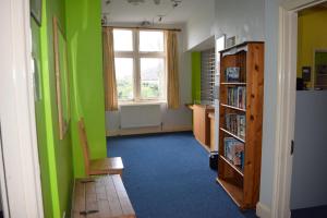 Habitación con paredes verdes, silla y estante para libros. en Kington Accommodation en Kington
