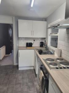 La cuisine est équipée de placards blancs et d'un four avec plaques de cuisson. dans l'établissement Cosy 2 Bedroom House, à Kent