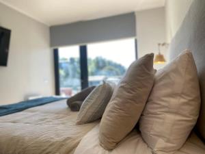 a group of pillows on a bed with a window at Depto 2D2B Frente a la Costanera Piscina Temperada Servicio HOM 0401 in Puerto Varas