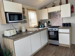 uma cozinha com armários brancos e um forno com placa de fogão em Comfy Cosy Caravan_Romney Sands em Littlestone-on-Sea