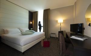 a hotel room with a bed and a woman standing in the window at H2C Hotel Milanofiori in Assago