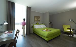 kobieta stojąca w sypialni z zielonym łóżkiem w obiekcie H2C Hotel Milanofiori w mieście Assago