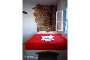 1 dormitorio con cama roja y pared de piedra en Politimis Studio N1 en Amorgós