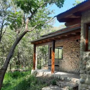 a stone house with a porch in the woods at Las Casitas del Pozo in Villa General Belgrano