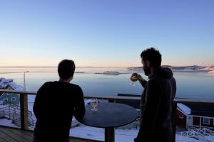 two men standing on a balcony with wine glasses at Hotel Hvide Falk in Ilulissat