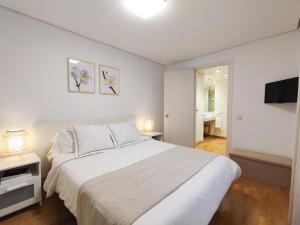 a white bedroom with a large bed and a bathroom at DFLAT Escultor Madrid Apartments in Madrid