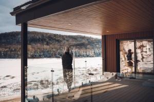 una persona parada en un porche mirando hacia la nieve en Lakeview Mid Century Luxury Cottage, en Sainte-Adèle