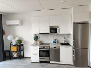 a kitchen with white cabinets and a stainless steel refrigerator at Valoisa huoneisto parvekkeella ja järvinäköalalla in Hämeenlinna