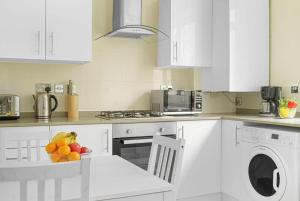 a white kitchen with a bowl of fruit on a table at Paddington with Balcony - CityApartmentStay in London