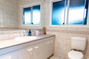 a bathroom with a sink and a toilet and two windows at Moffat Beach Retreat, Pet-friendly & Ocean Views in Caloundra