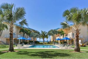 un resort con piscina, palme e ombrelloni di Seven Mile Beach Luxury 3BR Condo- Best Rates! a George Town