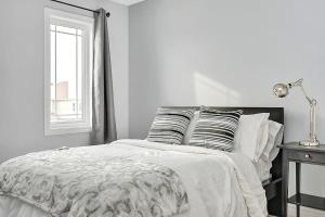 a white bedroom with a bed with pillows and a window at Modern townhome in Kanata w direct forest access in Ottawa