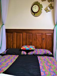 een bed met een houten hoofdeinde en een klok aan de muur bij Lake Victoria Country Home in Entebbe