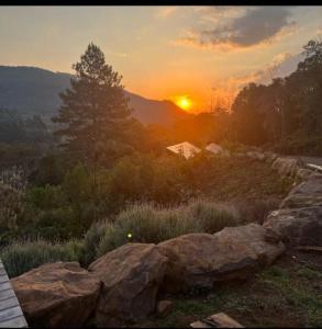 a sunset over a field with rocks and trees at Chalé PERTO DO CÉU em Gramado in Gramado