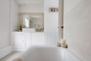 a white bathroom with a tub and a mirror at Country cottage in pretty village quay views in Chichester