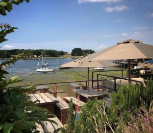 um restaurante com mesas e guarda-sóis e um barco na água em Idyllic countryside annexe near West Wittering beach em West Wittering