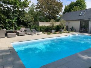 a large blue swimming pool with chairs and a house at The Salt House - Luxury Home with Pool & Hot Tub in Chichester