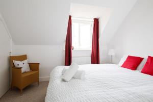 a bedroom with a white bed with red curtains and a chair at Lovely Selsey apartment with sea views sleeps 4 in Selsey