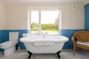 a bathroom with a tub and a toilet and a window at Stunning 5BR Home with Pool - 5 min to Beach in West Wittering