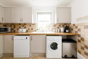 a kitchen with white cabinets and a washer and dryer at Lovely Seaside Villa & Gardens 40 Metres to Beach in Felpham