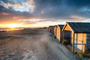 a row of beach huts on the beach at sunset at Gorgeous Shepherds Hut - Walk to Beach & Pub in West Wittering