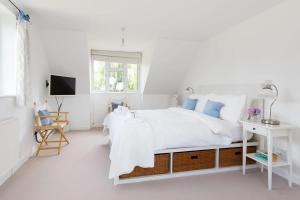 a white bedroom with a white bed and a television at Secluded rural retreat close to beach - sleeps 12 in Earnley
