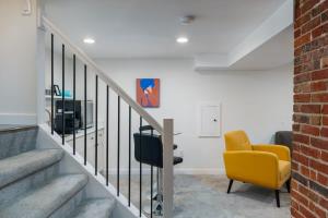 a living room with a yellow chair and stairs at Sleek & Stylish Apt Steps From Bluebird Theater in Denver