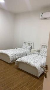 two beds in a room with white walls and wood floors at شاليه السمو الفندقي in Umm Lujj