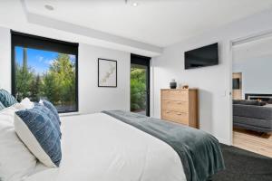 ein weißes Schlafzimmer mit großem Bett und Fenstern in der Unterkunft Cozy Coronet Peak Apartment at La Residence du Parc in Queenstown
