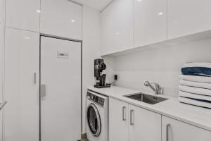 eine weiße Küche mit einer Waschmaschine und einem Waschbecken in der Unterkunft Lakeview Luxuy Vista Suite in Wanaka