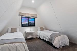 two beds in a white room with a window at MJ's Cottage Arrowtown in Arrowtown