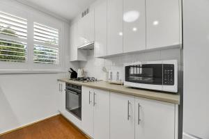 a white kitchen with white cabinets and a microwave at Hope St Cottage - Elegant & Cosy, Sleeps 6 in Bathurst