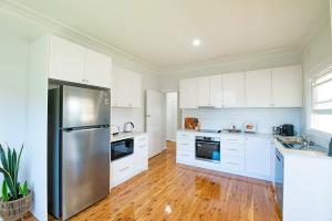a kitchen with white cabinets and a stainless steel refrigerator at Cobbora Cottage - Sleek & Stylish, Near Hospital in Dubbo +11 photos