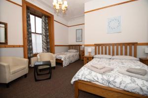 a bedroom with two beds and chairs and a chandelier at Alder Lodge Guest House in Lerwick
