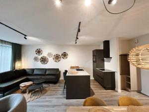 ein Wohnzimmer mit einem schwarzen Sofa und einer Küche in der Unterkunft Hello Zeeland - Appartement Duno Lodge I in Oostkapelle