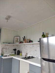 La cuisine est équipée de comptoirs blancs et d'un réfrigérateur en acier inoxydable. dans l'établissement Tiny house OMA, à Laguna Verde